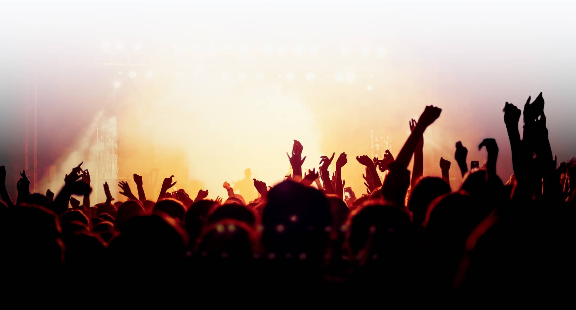 Crowd enjoying live music concert with raised hands and bright stage lights
